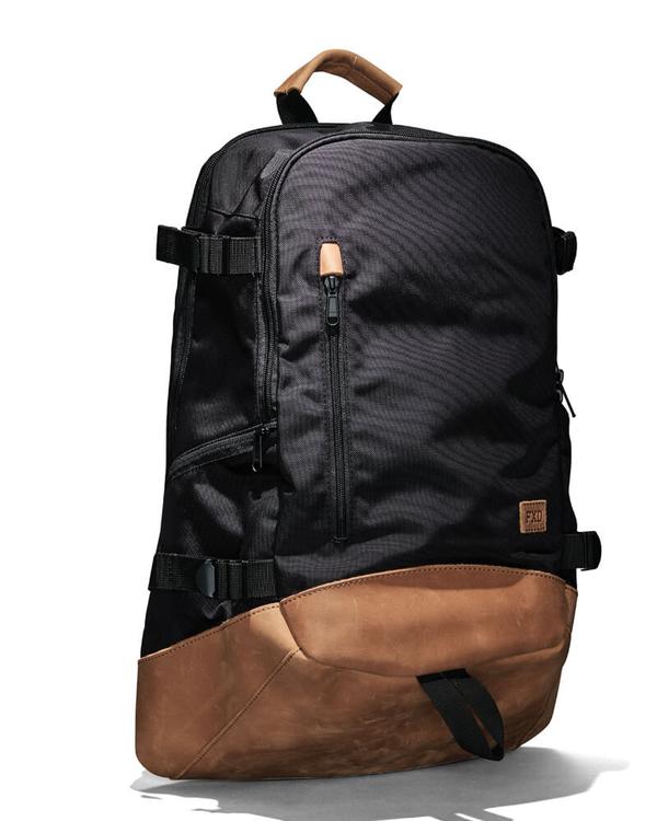 The FXD WBP-3 Work Backpack features a black and brown design with a leather base and Cordura Ballistic Fabric. It includes a front zippered pocket, adjustable side straps, and a top handle. Minimalist elegance is achieved through subtle stitching details.