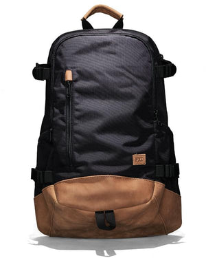 The FXD WBP-3 Work Backpack features black Cordura Ballistic Fabric, brown leather bottom and handle accents, a front zipper pocket, side straps, and a small leather "FXD" logo patch near the base.
