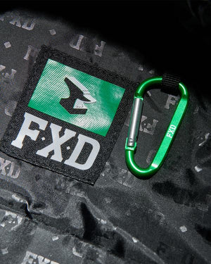 Close-up of a green "FXD" carabiner on a black Cordura Ballistic Fabric surface with a green and black label. The rugged design complements the FXD WBP-3 Work Backpack.