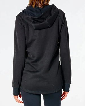 From the back, a person with long hair wears a Rip Curl Anti Series Flux II Zip black hoodie with the hood down, paired with black water-resistant pants. The background is plain white.