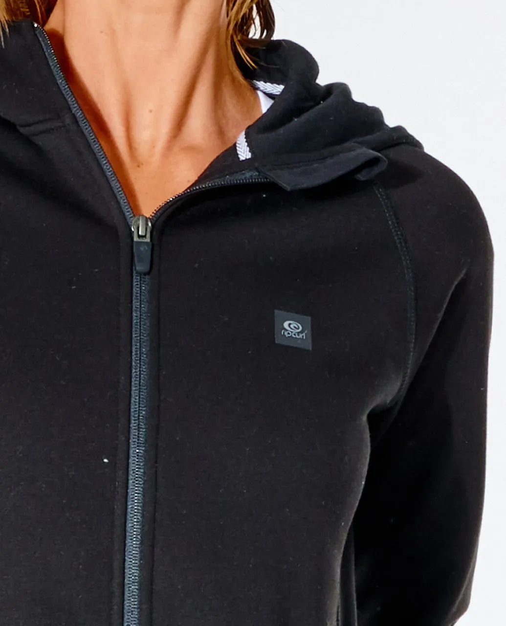 A person wearing a Rip Curl Anti Series Flux II Zip black hoodie with a logo on the chest. This winter wear boasts a water-resistant finish and front zipper, with the hood slightly visible, set against a plain white background.