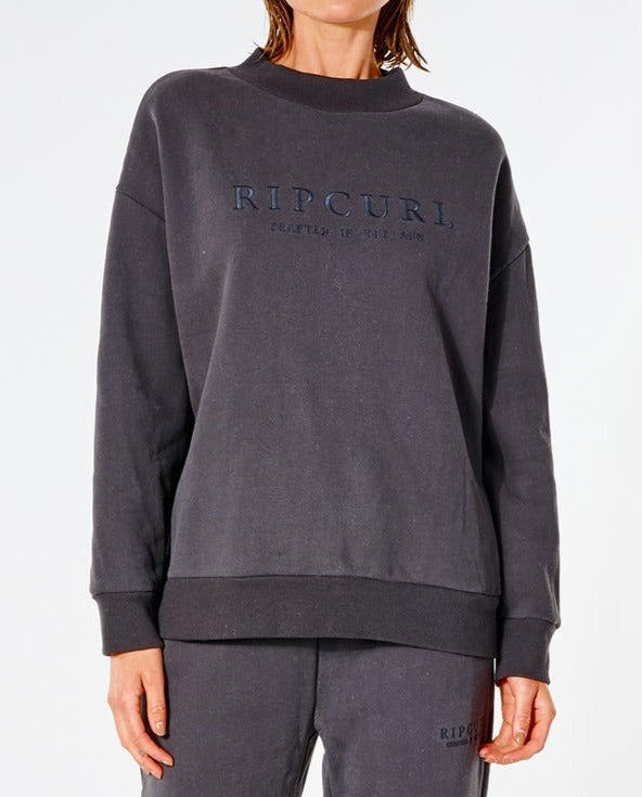 A person is wearing a dark gray Rip Curl Premium Surf Crew and matching pants, both featuring the phrase "Creatures of the Air." This casual outfit, with soft fleece lining, offers a relaxed fit ideal for laid-back occasions.