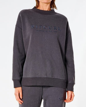 A person is wearing a dark gray Rip Curl Premium Surf Crew and matching pants, both featuring the phrase "Creatures of the Air." This casual outfit, with soft fleece lining, offers a relaxed fit ideal for laid-back occasions.