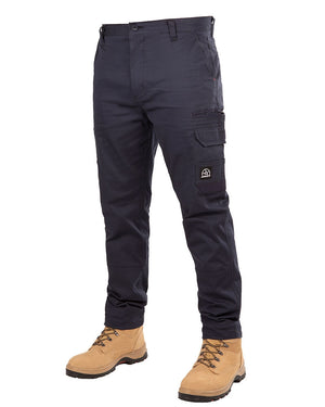 Image showing a person wearing UNIT Demolition Stretch Cargo Pants in navy blue, offering UPF 50+ protection, paired with tan work boots. The durable cargo pants feature multiple pockets, including a side cargo style pocket on the left thigh and two hand pockets. The lace-up boots have a rough texture suitable for outdoor or heavy-duty work.