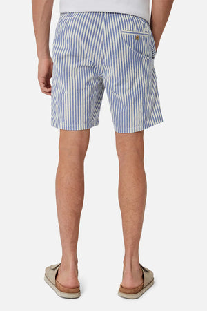 A man is shown from the back against a plain white background wearing Industrie The Laguna Short in blue and white stripes with an elastic waist, paired with a white shirt and beige sandals.
