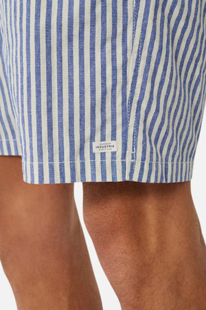 Close-up of a person wearing Industrie The Laguna Short, featuring blue and white vertical stripes and a label near the hem. The lightweight fabric and elastic waist offer comfort for warm weather. Only part of the legs is visible against a white background.