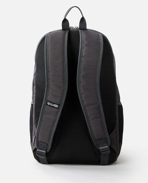 The Rip Curl Ozone 30L Multi Backpack in black is shown from the back, highlighting its padded shoulder straps and top carrying handle. The brand's logo is clearly visible on the left shoulder strap. Constructed from durable material with mesh padding for added comfort, it also includes a dedicated laptop section to keep your device secure.