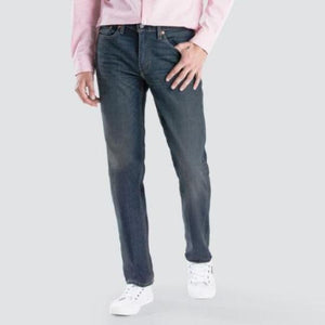 A person is standing against a gray background wearing a light pink long-sleeve shirt, stylish and comfortable Levis 514 Straight Jean, and white sneakers. Only the torso and legs are visible. One hand is placed in a front pocket, and the other hand is hanging by the side.