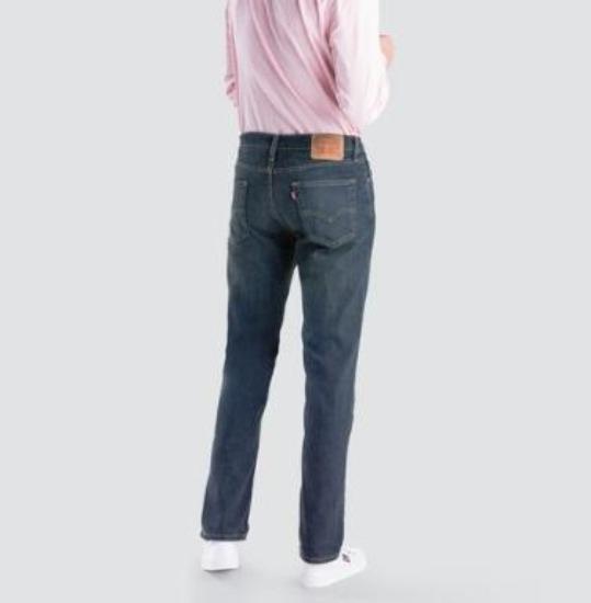 A person wearing stylish and comfortable Levis 514 Straight Jeans and a light pink shirt stands with their back facing the camera. They are also sporting white shoes, completing their look. The image is set against a plain light gray background, highlighting the straight leg cut of the jeans.