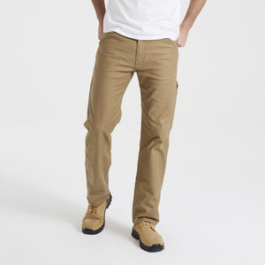 A person wearing Levis Workwear 505 Utility Pant in khaki and beige work boots stands against a plain white background. The individual is also sporting a white T-shirt, with their hands tucked into the durable pockets of their pants. The image centers on the lower half of the body.