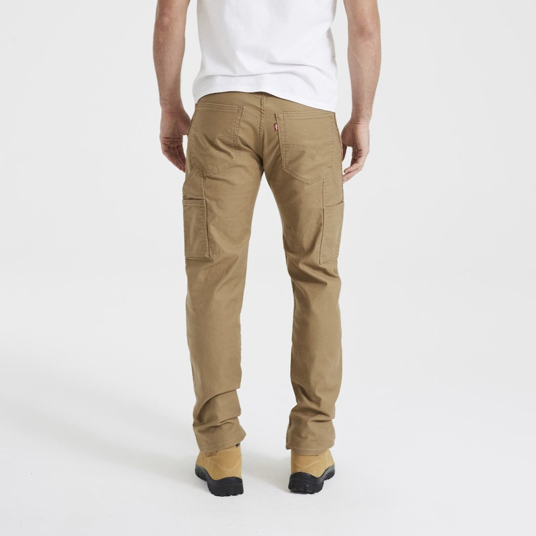 A person wearing a white t-shirt, khaki Levis Workwear 505 Utility Pants, and tan boots is standing with their back facing the camera. The image highlights the durable pockets of the work pants, showcasing multiple sturdy compartments.