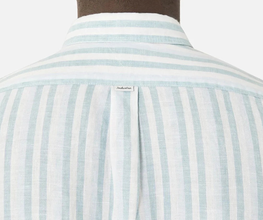 Close-up of the back of a person wearing a light blue and white striped Industrie The Linenman Shirt. The relaxed fit shirt features a small label beneath the button-down collar, with lightweight and breathable fabric.