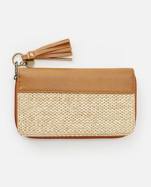 The Rip Curl Surf Gypsy Oversized wallet combines a brown leather upper section with a woven beige lower section. It includes a metal zipper with a removable leather tassel pull and features a metal ring adorned with a small round charm. The background is plain white.