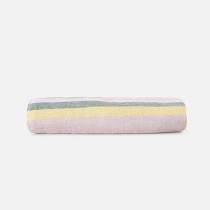 The Industrie The Maurepas Turkish Towel is a rolled-up beach towel made from soft cotton with pastel stripes in muted pink, yellow, blue, and green on a light gray background.