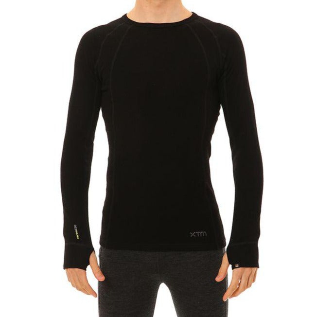 A person wearing the XTM Merino Long Sleeve Top, a fitted, long-sleeved thermal top in black with a round neckline and odour repellent properties, along with dark-colored pants is shown against a white background. The person has their arms relaxed by their sides, and the image primarily highlights the clothing.
