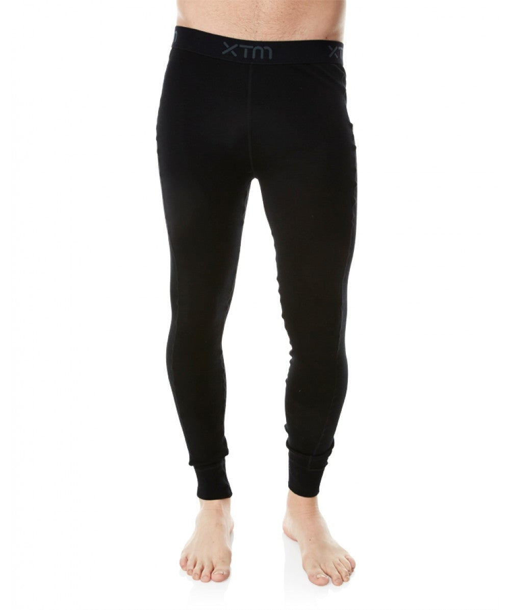 A person standing on a white background is wearing XTM Merino Pant thermal leggings, made from Australian Merino Wool, which extend to their ankles. The black leggings feature an elastic waistband with the "XTM" logo visible and have odour-repellent properties. The person's upper body and feet are bare.