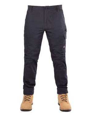 A person is wearing durable UNIT Demolition Stretch Cargo Pants in navy blue with multiple pockets and tan work boots with light brown laces. The slim-fit pants, featuring UPF 50+ protection, create a practical yet stylish look. The person's hands are not visible in the white background image.