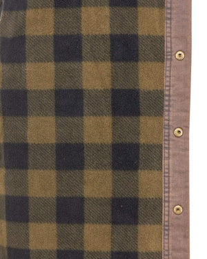 A close-up of fabric reveals a green and black checkered pattern on the left, like the Outback Loxton Jacket. The right side displays a tan border with metallic snap buttons, evoking the water-resistant style often found in rugged apparel.