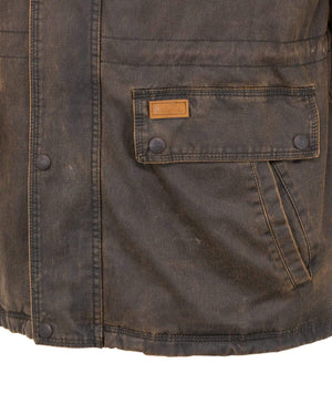 A close-up view of the Outback Ranchers Jacket showcases its weathered brown, hard-wearing fabric with buttoned pockets on the right side and visible stitching details. The material shows signs of wear, and there is a small rectangular leather patch sewn above the pocket, hinting at its previous adventures.