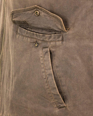 Close-up of the Outback Landsman Vest's pocket area, showcasing two pockets with button details. The top pocket features a flap with one button and is partially open, revealing the interior. The bottom pocket is a simple slit pocket with visible stitching. The machine washable fabric has a weathered look.