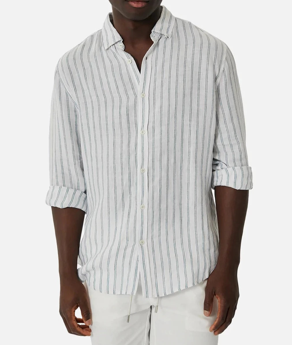 A man in the Industrie The Paglia Long Sleeve Shirt, with rolled-up sleeves and relaxed fit light gray stripes, pairs it with white pants against a plain white background.