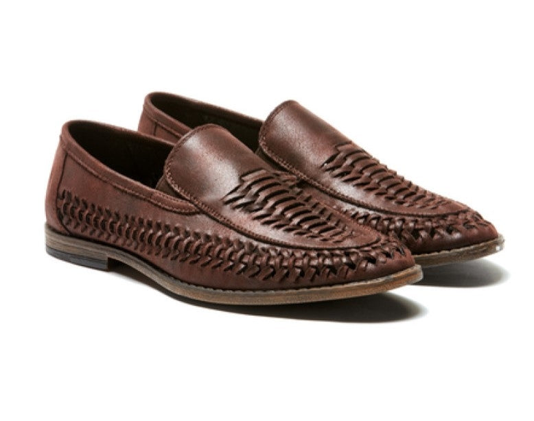 Introducing the UNcut Lake Shoe: A pair of brown woven leather loafers featuring an intricate braided pattern on the upper and sides. These casual yet comfortable shoes boast a rounded toe, a slight heel, and a slip-on design, beautifully combining traditional craftsmanship with modern style.