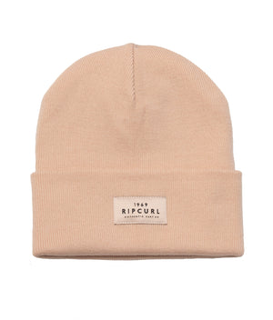 The Rip Curl Premium Surf Beanie is a beige rib knit hat with a folded brim, featuring a small rectangular patch on the front that reads "1969 RIP CURL, A PRODUCT OF THE SEARCH" in black lettering.