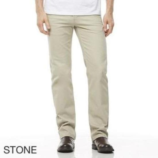 A person is wearing the Riders Straight Moleskin Stretch pants in light beige, labeled "STONE," while standing with their legs slightly apart. The individual pairs the pants with a white shirt and dark brown shoes. Only the lower half of their body is visible against a plain white background.