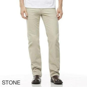 A person is wearing the Riders Straight Moleskin Stretch pants in light beige, labeled "STONE," while standing with their legs slightly apart. The individual pairs the pants with a white shirt and dark brown shoes. Only the lower half of their body is visible against a plain white background.