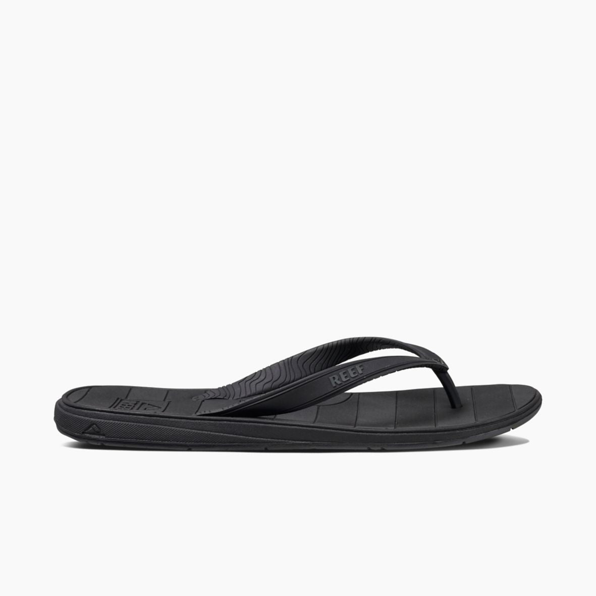 The REEF Switchfoot LX is a black flip-flop sandal featuring a sleek design and textured straps, with the brand name "Reef" prominently displayed on the straps. The comfortable and supportive sole has horizontal lines for added grip and arch support, made with a rubber sponge footbed, making it ideal for everyday wear.