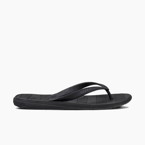 The REEF Switchfoot LX is a black flip-flop sandal featuring a sleek design and textured straps, with the brand name "Reef" prominently displayed on the straps. The comfortable and supportive sole has horizontal lines for added grip and arch support, made with a rubber sponge footbed, making it ideal for everyday wear.