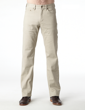 A person stands against a plain white background, wearing the chic Riders Straight Pant Stretch in beige and polished brown leather shoes. The person's hands and upper body are not visible in the image. The straight-legged pants offer a sophisticated look, while the shoes have a refined appearance.