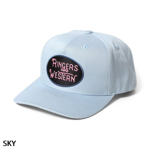 The Ringers Western Truckstop Baseball Cap comes in light blue and features a curved brim. It also has an oval-shaped patch on the front that displays "Ringers Western" in pink text on a black background, with "SKY" written in black at the bottom left corner. The cap includes an adjustable strap to ensure a perfect fit.