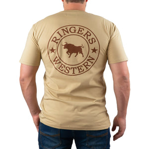 A man is wearing the Ringers Western Signature Bull Classic T-Shirt in beige, which features a comfortable crew neck design. On the back, there's a circular emblem with a bull in the center, surrounded by the text "RINGERS WESTERN" and two stars. The man is facing away from the camera and is also dressed in blue jeans.