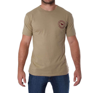 A person wearing a comfortable, plain beige Ringers Western Signature Bull Classic T-Shirt with a small maroon circular logo on the left side of the chest and blue jeans is standing with arms relaxed by their sides. The background is plain white.