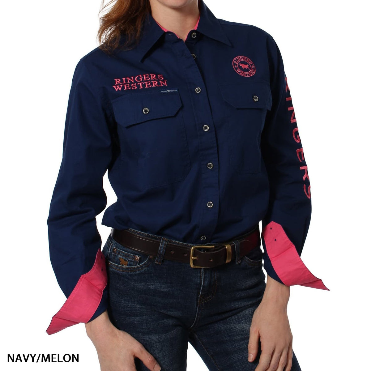 A woman wears the Ringers Western Signature Jillaroo Womens Full Button Shirt in navy with pink accents, "RINGERS WESTERN" embroidered on the chest and sleeve, pink cuffs and collar lining, paired with jeans. Made from 100% cotton.
