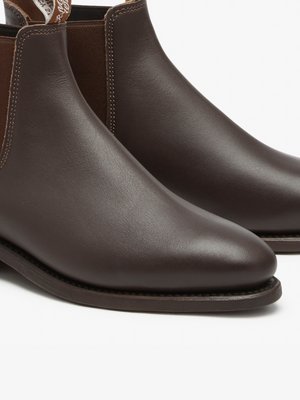 Close-up of RM Williams Adelaide Rubber Sole Boots in brown leather with elastic side panels and stitching details. Visible soles highlight their sleek design and smart-casual appeal.