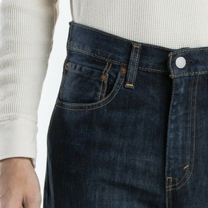 A person wearing a white, long-sleeve, waffle-knit shirt and dark blue Levis 516 Straight Jean. The jeans feature prominent stitching on the pockets and waistband, with a visible button and belt loops for a comfortable fit. Made from 100% cotton, the person's left hand rests at their side.
