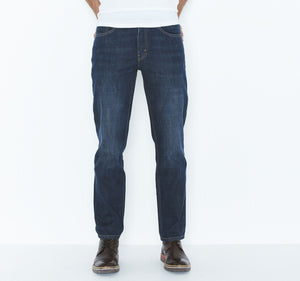 A person wearing dark blue Levis 516 Straight Jeans and brown leather shoes stands against a plain white background. The image is cropped just below the waist, showcasing only the comfortable fit from the lower torso to the legs. A white shirt is partially visible at the top.