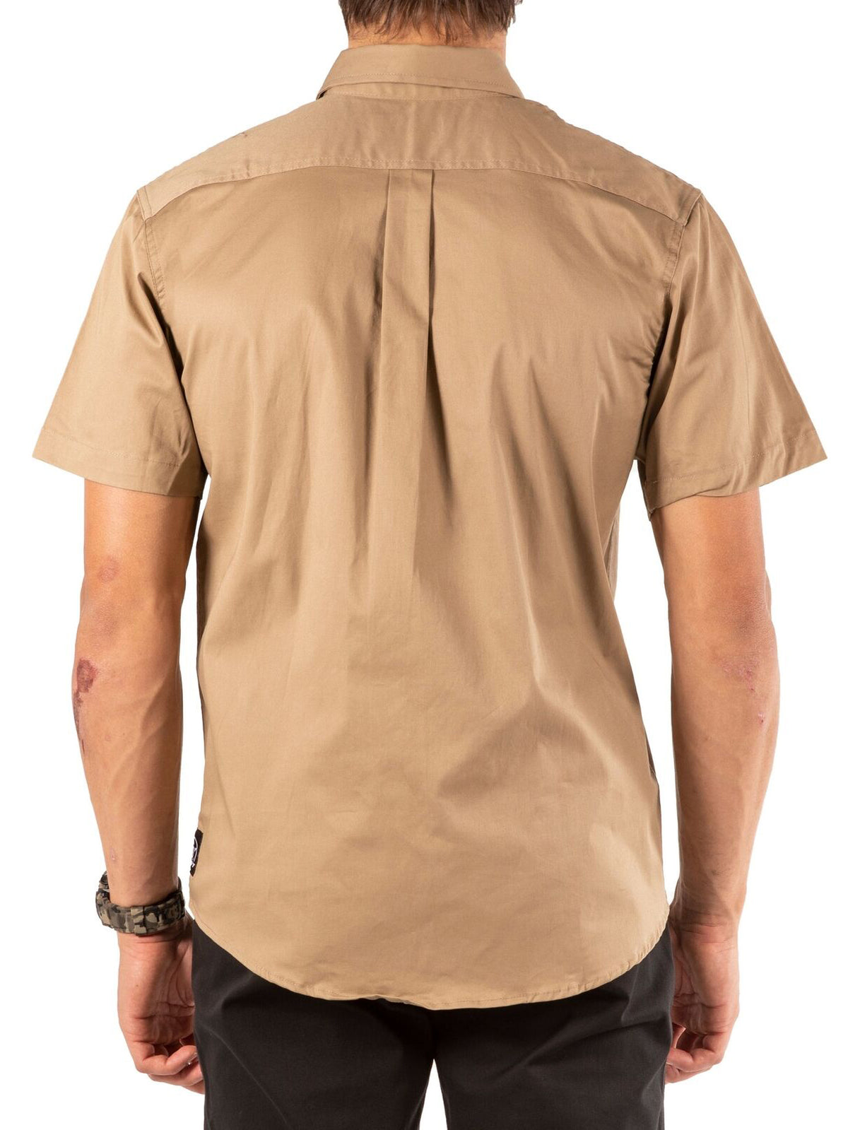A person is shown from the back against a white background wearing the UNIT Craftman Stretch Short Sleeve Shirt in light brown and black pants.