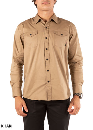 A person wears the UNIT Craftman Stretch Shirt—a long-sleeve, button-up khaki work shirt with cotton stretch and two chest pockets—paired with black pants, standing before a white background. "KHAKI" appears in the bottom left.