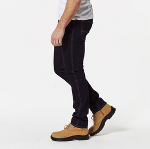 A person is standing, showing their side profile from the shoulders down. They are wearing black Levis Workwear 511 Slim Jeans, beige work boots with black soles, and a white shirt. The background is plain white.