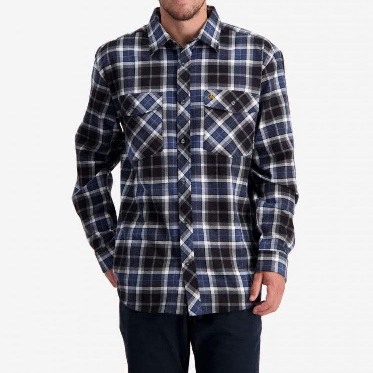 A person is wearing a Swanndri Egmont Full Button Flannelette shirt from the Twin Pack, featuring long sleeves, a button-up design, and a plaid pattern in black, white, and blue tones made of 100% brushed cotton. The shirt includes two chest pockets with one adorned by a small logo. The individual is also dressed in dark pants; their face is not visible in the image.
