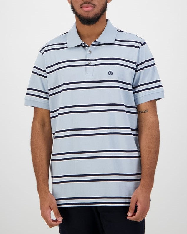 A person with short hair and a beard is wearing a casual, light blue, short-sleeved Swanndri Lincoln Stripe Polo made from 100% cotton. The shirt features horizontal white, black, and blue stripes. They are standing against a plain white background.