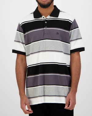 A person is seen against a plain backdrop wearing a Swanndri Kingfield Stripe Polo, which is short-sleeved and made from 100% cotton, in black, gray, and white stripes. The shirt features a collar with buttons at the top. The person's face is not visible.