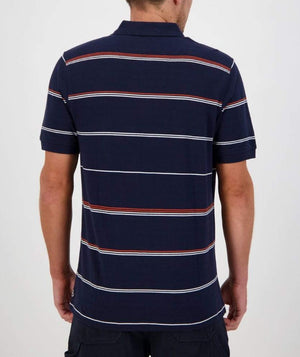 A person is wearing a Swanndri Concord Stripe Polo, characterized by its navy blue short sleeves and horizontal white and red stripes. Featuring the distinct Swanndri logo, they stand with their back to the camera, arms slightly bent at the elbows. The background is plain and light-colored.