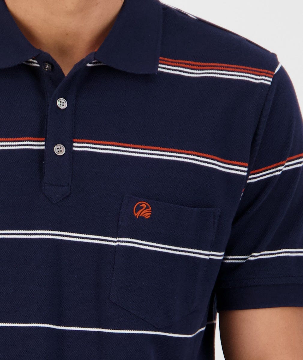 A close-up of a person wearing the Swanndri Concord Stripe Polo, featuring navy blue with white and red horizontal stripes. This 100% cotton polo shirt includes a small chest pocket on the left side, embroidered with an orange Swanndri logo. The collar has two visible buttons.