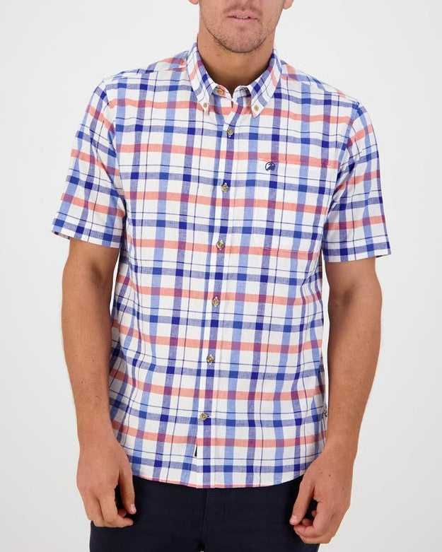 A person is wearing the Swanndri Taunton Shirt, a classic fit, short-sleeved button-up featuring a checkered pattern in blue, red, and white colors. The comfortable shirt has a small embroidered logo on the chest. They are standing against a white background with their arms relaxed by their sides.