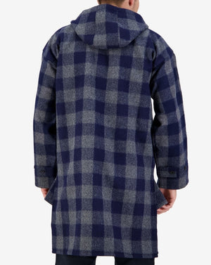 A person is wearing the Swanndri Original Lace Front Bush Shirt, a long, hooded coat in blue and gray checkered plaid made of 100% wool. The shirt features buttoned cuffs and is shown from the back, emphasizing its weatherproof design and impressive length.