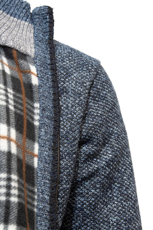 Close-up of a shoulder in a textured knit Sugar Kendry Full Zip Polar Fleece Cardigan, dark blue with ribbed details, over a gray and white plaid shirt with brown stripes. The zipper adds functionality to this stylish ensemble, ideal for layering on cooler days.